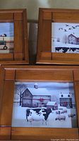Three pine framed country cow prints with rustic barn and farm scenes, each approx 12x12 inches.