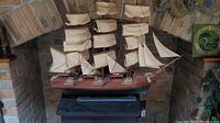 Front view of the large model sailboat showing multiple beige sails and detailed rigging, sitting in a brick alcove.