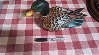 Front angle showing carved and painted wooden duck on plaid tablecloth alongside a black Sharpie marker for size reference.