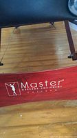 Close-up image of wooden frame showing Master Massage Equipment Chicago logo in white on reddish wood.