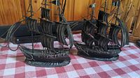 Two metal ships displayed on a checkered cloth background, showing both ships side by side with detailed sails and flags.