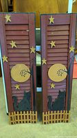 Front view of both wooden decorative window shutters leaning side by side. Shows full painted design and condition.