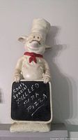 Front view of resin pig chef statue holding chalkboard with written specials.