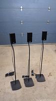 Full set of three black BOSE speakers on stands with rectangular metal bases, photographed against a blue garage door.