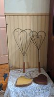 Two wire heart shaped rug beaters standing upright against a wall, showing wooden handles and wire frames