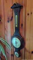 Full view of the wooden barometer mounted on a wooden wall showing length and shape.