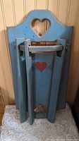 Folded wooden clothes hanger showing heart-shaped cutout and decoration on painted blue wood.
