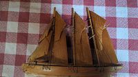 Front view of the handmade wooden ship model showing three triangular sails constructed of wood and wire rigging, placed on a checkered cloth background.