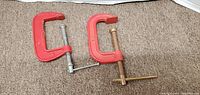 Two large red vintage C-clamps laid on carpet, showing silver and brass screw mechanisms