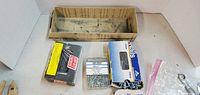 Three boxes containing assorted nails and screws, including a wooden box and two packaged boxes.