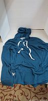 Blue ladies' hoodie with tunic neck and white drawstrings shown laid flat on a surface