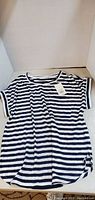 Blue and white striped blouse laid flat showing full front view with tags attached.