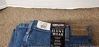Folded Kirkland blue jeans with original tags visible showing size 36x32 and brand information.