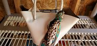Front view of white textured handbag with animal print and green patterned scarf tied to handle on metal rack shelf.