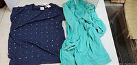 Two ladies tops displayed flat, navy blue short sleeve top with colorful dots and aqua long sleeve top with lace detail.