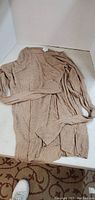 Light brown knitted long sleeve ladies sweater laid flat showing overall shape and texture.