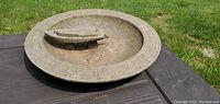 View of the top side of the birdbath showing the metal boat figurine on a round plate with Roman numeral markings.
