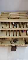 Top view of open fishing tackle box showing multiple tray compartments for fishing gear.