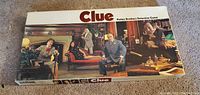 Top view of the vintage Clue board game box with classic illustration showing characters inside a mansion room.