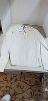 White long sleeve ladies sweater laid flat showing front side and tags