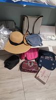 Photo showing assortment of handbags and wide-brim straw hat arranged on floor near bed