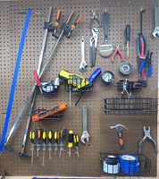 Wide photo of organized pegboard with clamps, screwdrivers, pliers, measuring tape, hammer and small tools in wire baskets.