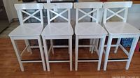 Front view of four white painted wood kitchen counter stools with X-back design