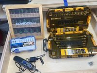 Dremel rotary tool, charger, Dremel bit set, Kowood Pro router bits in wooden and glass case, two DeWalt socket sets in black and yellow plastic cases