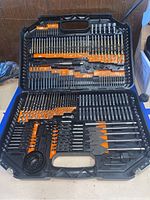 Full open carrying case showing organized drill bits, hole saws, screwdriver bits, and accessories with orange labels in molded slots.
