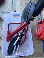 Two disassembled kayak paddles, red hand pump inflator, and clear plastic tote bin on the floor.