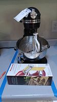 Black stand mixer on countertop with bowl and panel-mounted attachments.