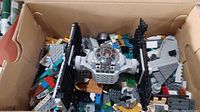 Box with partially assembled Lego Star Wars TIE Fighter and loose Lego pieces inside.