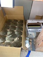 Full view of box containing multiple coils of collated nails, a box of black strip nails, and metal brackets on wooden surface.