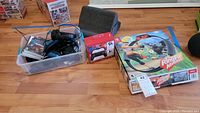 Plastic box containing multiple Nintendo Switch game cases, controllers, headsets and cables, next to boxed Ring Fit Adventure game and a new controller box