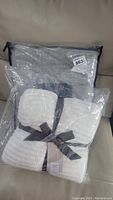 Photo of both throws in clear plastic bags, showing the gray Pendleton throw and white West Elm chenille rib throw tied with ribbon.