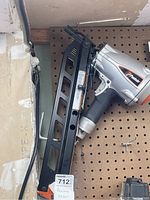 Paslode pneumatic nailer hanging on pegboard showing nail magazine and part of tool body with orange branding.