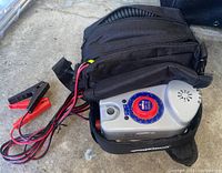 Power inflator partially packed in a black soft carrying case with cables and clamps visible on concrete floor