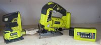 Ryobi cordless sander with dust bag and battery pack shown on wooden surface against light wall background.
