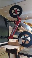 Side angle of full red Strider balance bike with black plastic wheels and tires, showing frame and tires.