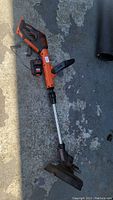 Full view of the Black & Decker cordless string trimmer showing orange and black color, silver shaft, and protective guard near the cutting head.