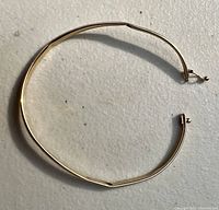 Top-down view of the thin, open bangle bracelet showing its slightly bent circular shape and clasp intact.