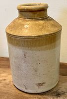 Full view of the antique crock showing its two-tone glazed surface, body shape, and rim design.