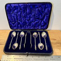 Full set of six spoons and a pair of tongs in fitted case with blue velvet and satin lining.