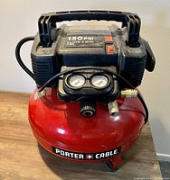 Front view of the red Porter Cable air compressor with top handle, pressure gauges, and hose attachment visible.