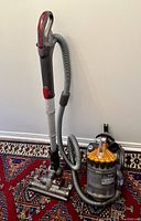 Full side view of Dyson DC23 vacuum cleaner showing canister, hose, wand, and floor head on a patterned carpet.
