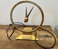 Front view of clock showing circular floating dial, hands, and gold-tone metal base