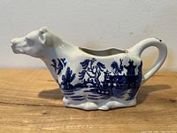 Side view of the cow creamer showcasing flow blue Willow pattern with pagodas and trees.