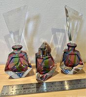 Front angle view of three multi-colored vintage glass perfume bottles including an atomizer in the center with clear geometric stoppers on the side bottles.