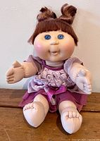 Front view of the Cabbage Patch Kids doll showing hairstyle, face with blue eyes, and pink dress with fabric roses and satin ribbon.