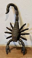 Front view of the vintage cast iron scorpion showing segmented curved tail, eight legs, two claws, and textured body detail.